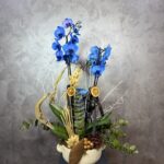 Derin Flowers tarafından sunulan 'Mavi Orkide' ürününün, seramik saksıda sunulan mavi orkideler ve sarı çiçek detaylarıyla hazırlanmış şık çiçek aranjmanı.