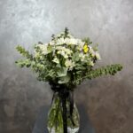 Derin Flowers’ın 'Vazoda Papatyalar' aranjmanı; cam vazo içinde beyaz papatyalar, yeşil yapraklar ve sarı tonlarda küçük çiçeklerle hazırlanmış doğal ve ferah bir çiçek buketi.