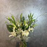 Derin Flowers’a ait 'Vazoda Lilyum Aranjmanı'; cam vazoda sunulan beyaz lilyumlar, yeşil yapraklar ve zarif çiçek dokunuşlarıyla hazırlanmış şık bir çiçek buketi.