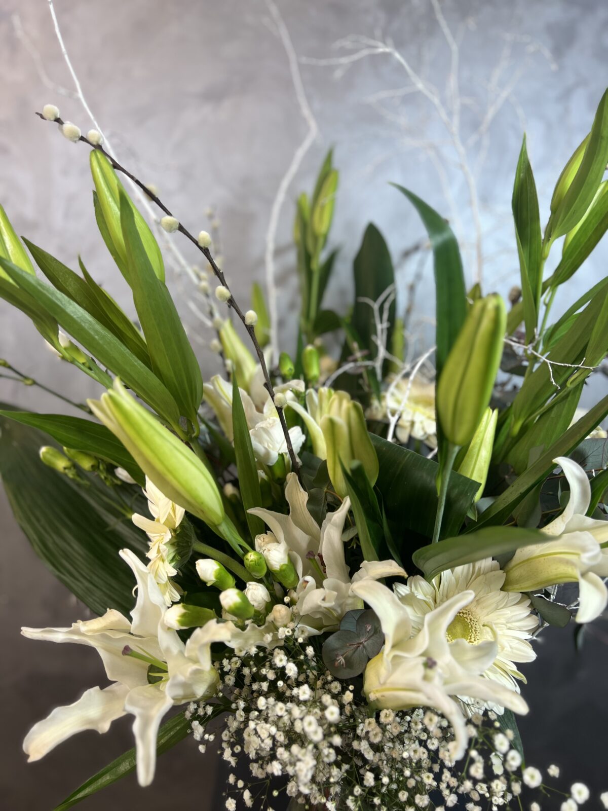 Derin Flowers'ın 'Vazoda Lilyum Aranjmanı' ürününün yakın plan görüntüsü; zarif beyaz lilyum çiçekleri ve yeşil yaprak detaylarıyla cam vazo içerisindeki şık çiçek buketi.