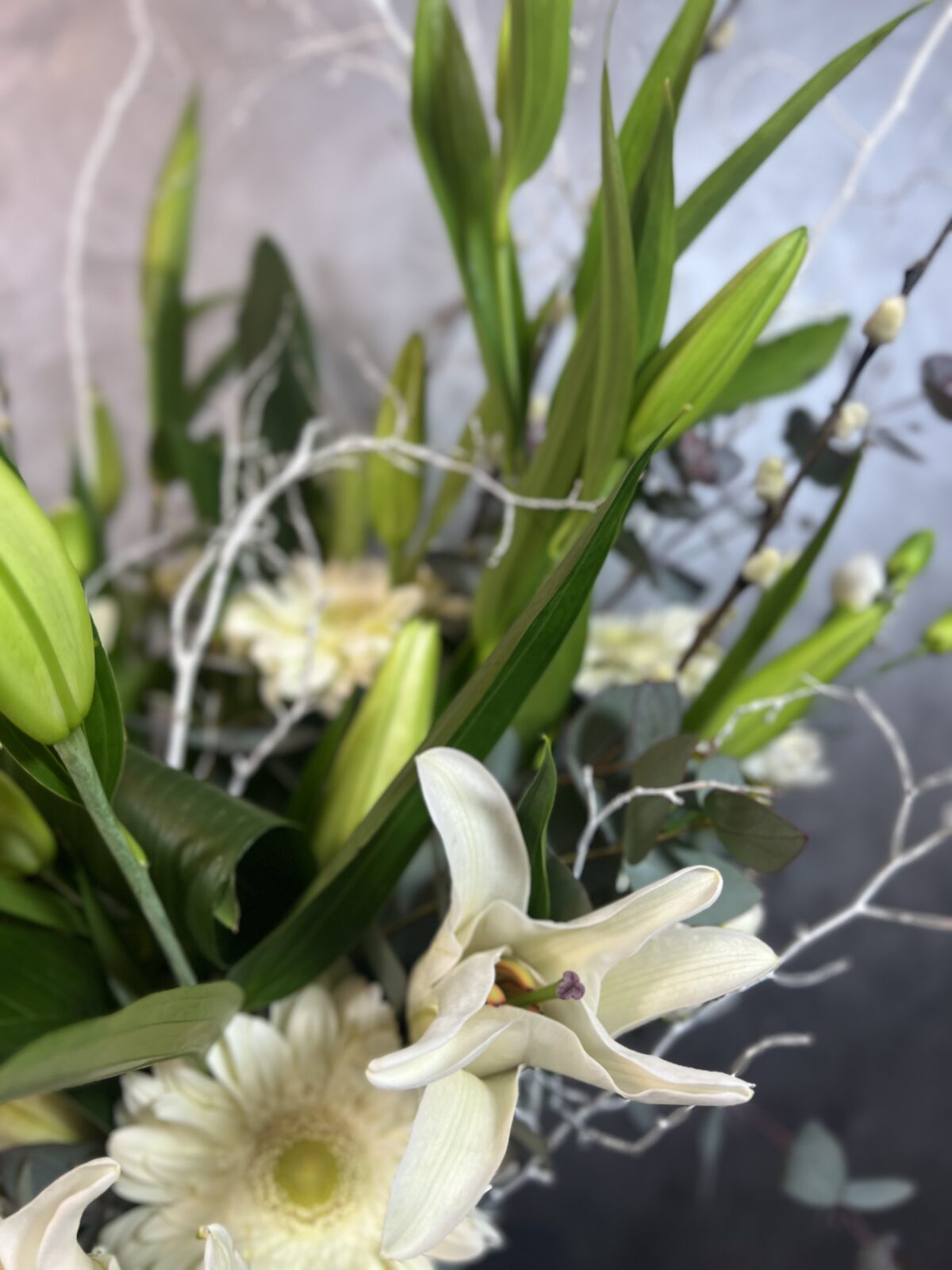 Derin Flowers'ın 'Vazoda Lilyum Aranjmanı' ürününün yakın plan görüntüsü; zarif beyaz lilyum çiçekleri ve yeşil yaprak detaylarıyla cam vazo içerisindeki şık çiçek buketi.